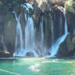 Uitzicht op de Kravica-watervallen in Bosnië en Herzegovina, omringd door weelderig groen en een helderblauwe rivier